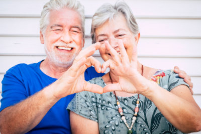 elderly couple smiling and forming a heart with their hands