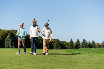 friends walking with golf clubs on green field